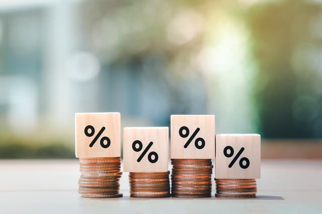 Imagem com pilhas de moedas de diferentes tamanhos e quarados com símbolo de percentual. Foto: Getty Images