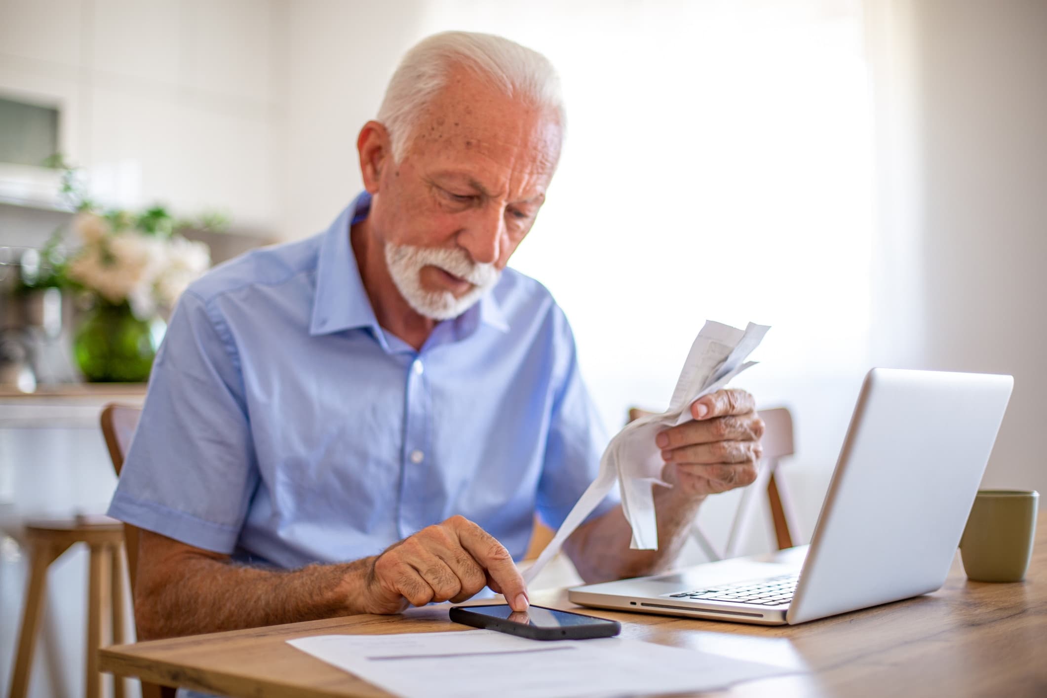 Homem idoso fazendo contas utilizando computador, celular e papéis. Foto: Getty Images.