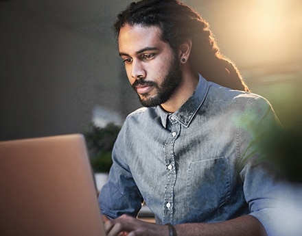 Homem de barba e camisa azul utilizando seu notebook