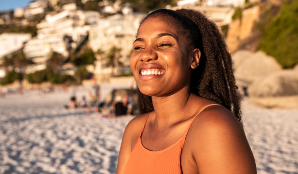 Mulher sorrindo em uma praia, com raios de sol batendo em seu rosto