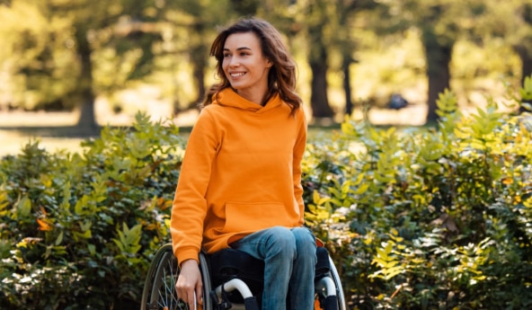 Mulher vestindo uma blusa laranja, em uma cadeira de rodas, sorrindo