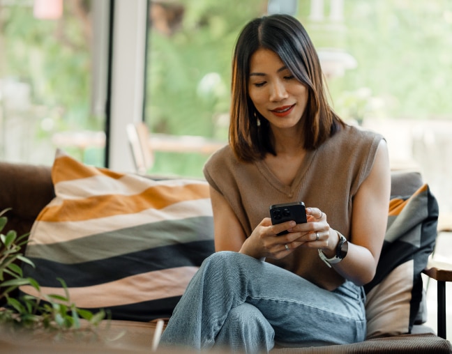 Senhora sorrindo com celular na mão esquerda e uma xícara na mão