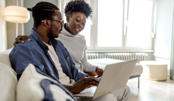 Homem e mulher sentados no sofá mexendo no notebook