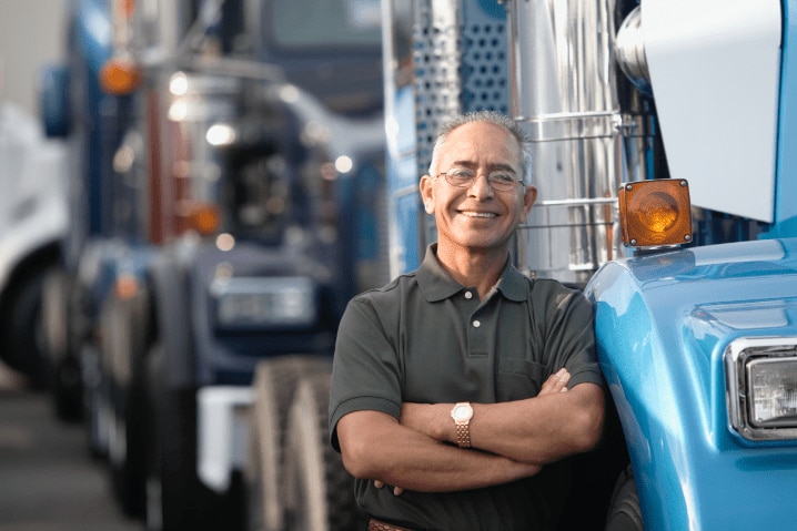 senhor de braços cruzados sorrindo ao lado de um caminhão azul