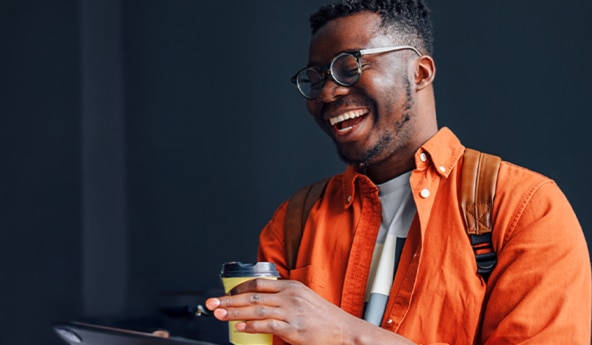 Cliente Itaú Uniclass sorrindo enquanto segura um copo térmico, com uma mochila nas costas e utilizando óculos